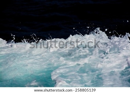 Azure and white boat wake seafoam with white splashes, sprays and drops on dark blue background abstract