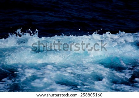 Azure and white boat wake seafoam with white splashes, sprays and drops on dark blue background abstract