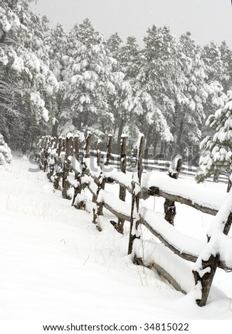 A rural snow covered post rail fence line disappears in the distant treeline during a snow storm.