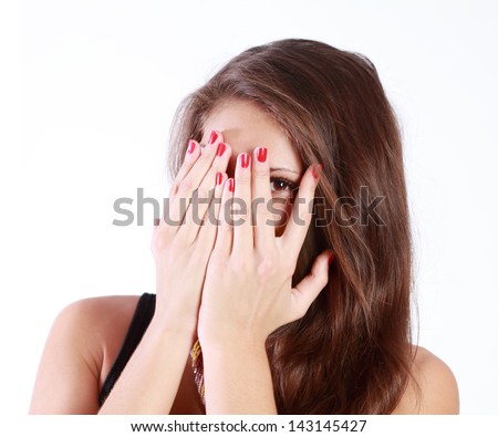 Young woman hides her face in her palms and spies isolated on white background.