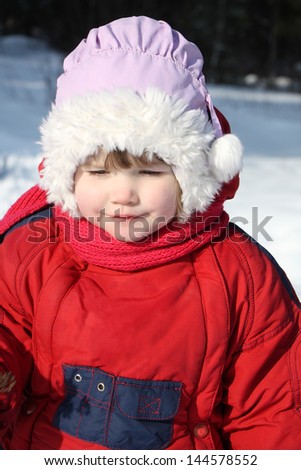 Little beautiful girl wearing warm clothing walks in winter forest