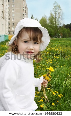 Cute little girl wearing white panama and blouse holds yellow dandelions