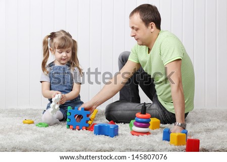 Happy little daughter and her father play toys on soft carpet at home.