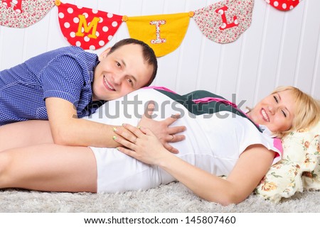 Happy pregnant wife and husband lie on carpet and man listens belly.