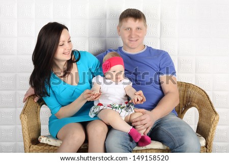 Young father, beautiful mother and cute baby sit on wicker sofa at home.