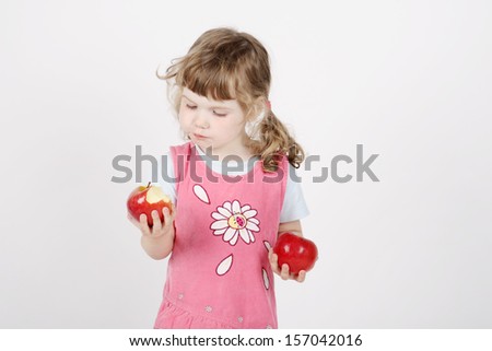 Little beautiful girl in pink eats apple and holds second apple in hand on white background.