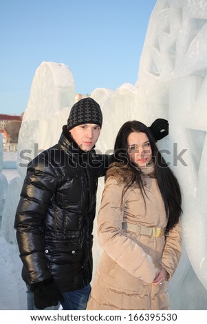 Young happy boy and girl stand near big ice wall at winter day.
