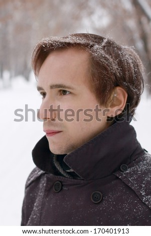 Young man with snowflakes in hair looks at distance outdoor at winter snowy day