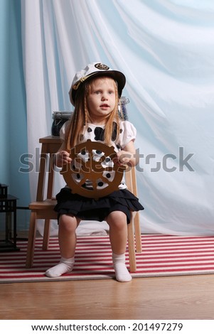 Little beautiful girl sits with steering wheel and plays sailor in studio with decorations
