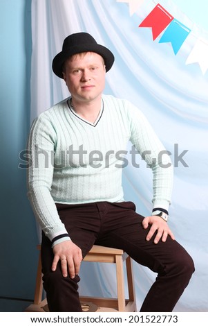 Handsome smiling young man in black hat sits and poses in studio