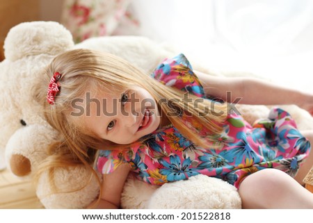 Pretty little girl lies on big soft toy bear and looks at camera in studio
