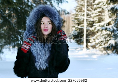 Beautiful girl in fur coat dreams and looks away in winter forest