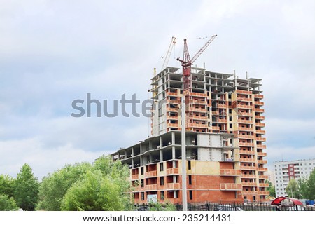 Unfinished high-rise apartment building with brick walls and crane at summer