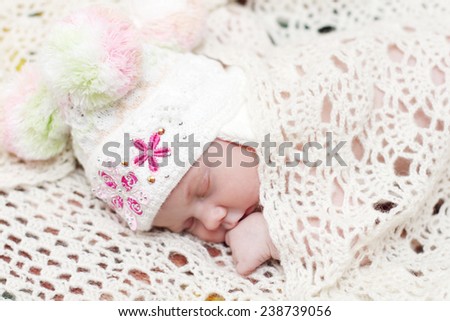 Baby in hat lies on bed under soft white knitted shawl and sleeps