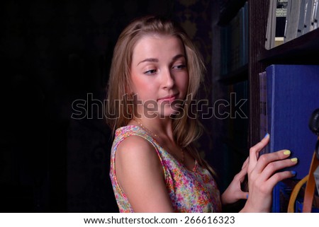 Closeup beautiful girl with long blond hair takes book from shelf