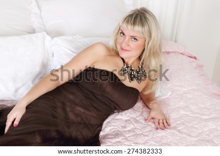 Beautiful woman in long dress lies on bed with pink linen in white room