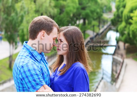 Young woman and man in blue touch noses in summer park with small river