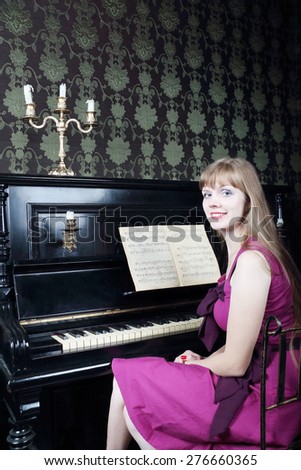 Pretty young woman sits in room near piano, smiles and looks at camera