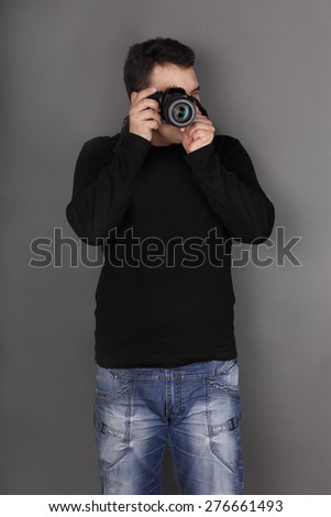 Handsome young man in jeans with modern camera shoots in grey studio