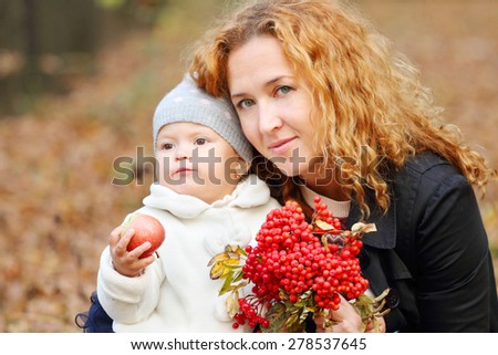 Woman with little daughter and rowanberry in autumn park at sunny day. Focus on mother