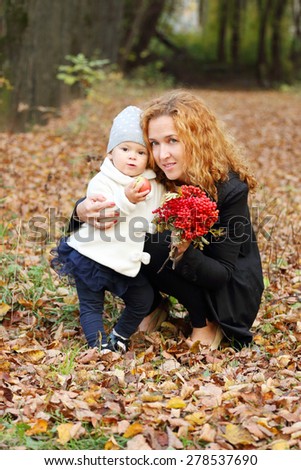 Beautiful woman with little daughter and rowanberry in autumn park at sunny day