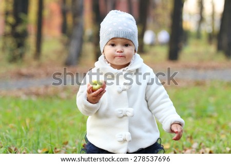 Little cute girl in white holds apple and walks in autumn park