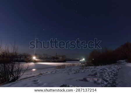 Path near frozen river covered with snow at night and beautiful starry sky