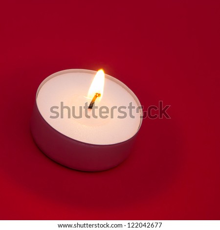 Lit tea light on red background with copy space