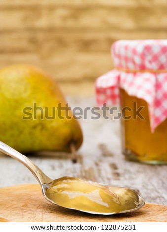 Homemade pear jelly on spoon with jar and fruit in background