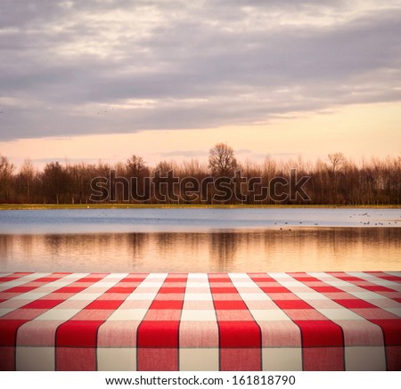 Picnic table template with red checkered tablecloth on sunset lake background