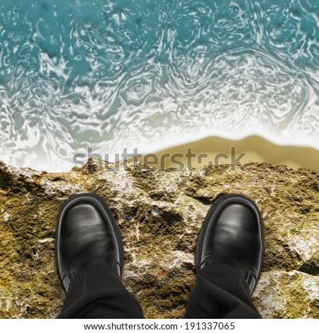 On the edge concept with man standing on cliff ledge looking down at ocean