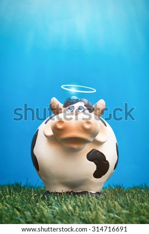 Ceramic cow with halo standing in grass on clear blue sky with light from above