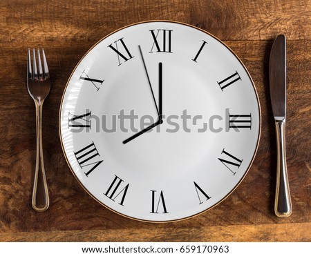 Eight hour feeding window concept or breakfast time with clock on plate and knife and fork on wooden table, overhead view