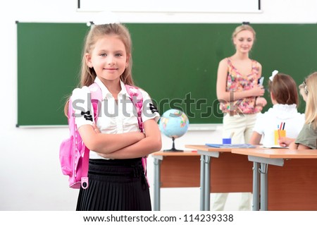 portrait of schoolgirl with a school backpack, in the background a classroom and the teacher tells the class
