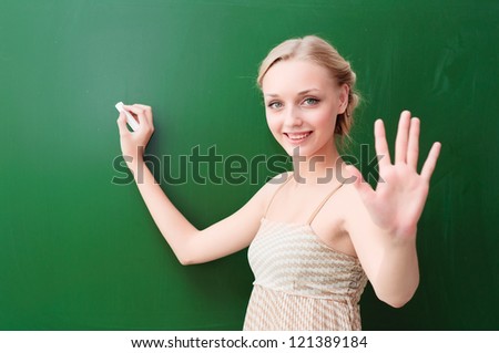 young beautiful teacher writes on the blackboard with chalk and shows five points