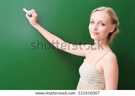 young beautiful teacher writes on the blackboard with chalk