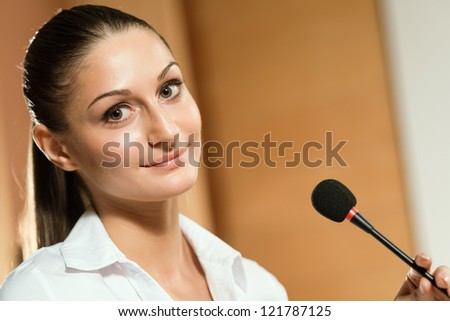 attractive woman standing near a microphone, preparing a speech, looking at the camera
