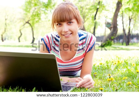 beautiful young woman working with laptop in the park on the grass