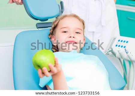 girl in the dentist\'s chair shows a green apple, regular care of your teeth