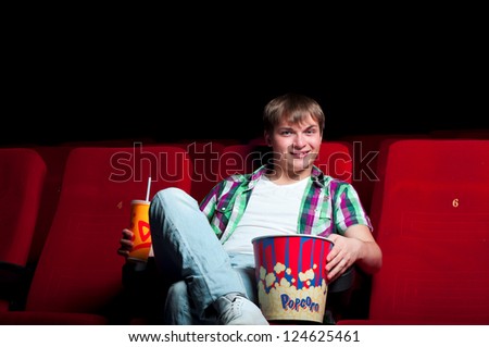 man in a movie theater, watching a movie and drink a drink