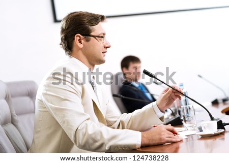 Portrait of a businessman, said into the microphone, in the background colleagues communicate with each other