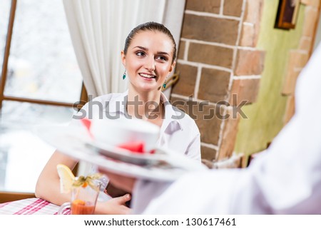 waiter brings a dish for a nice woman at the restaurant, she looks at him and smiles