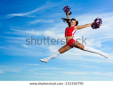 Young cheerleader in red costume jumping against blue sky