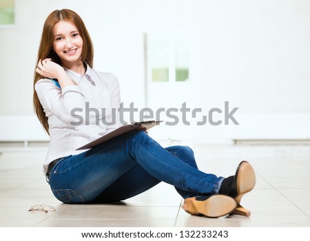 Portrait of an attractive woman sitting on the floor cross-legged and holds the tablet for notes
