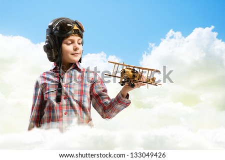 Boy in helmet pilot playing with a toy wooden airplane in the clouds, dreaming of becoming a pilot