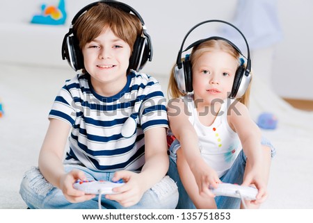 cute boy and girl playing gaming console in wireless headphones, sitting on the floor