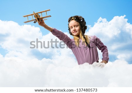 girl in helmet pilot playing with a toy wooden airplane in the clouds, dreaming of becoming a pilot