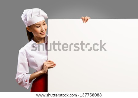 female chef holding a poster for text, look at the poster and smiling