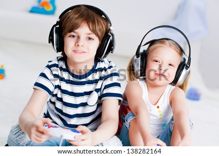 cute boy and girl playing gaming console in wireless headphones, sitting on the floor