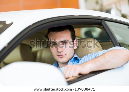portrait of a man sitting in a sports car in the showroom, make expensive purchases